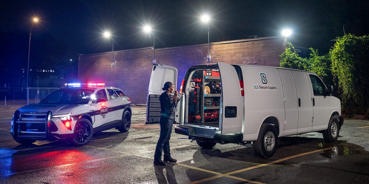 A police officer parked with their lights on next to a Chevrolet Express Cargo Van that was located with stolen vehicle assistance.