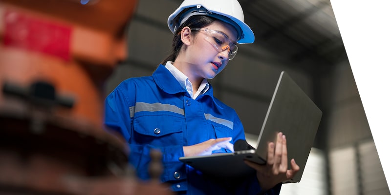 A worker on their computer in a hard hat. 