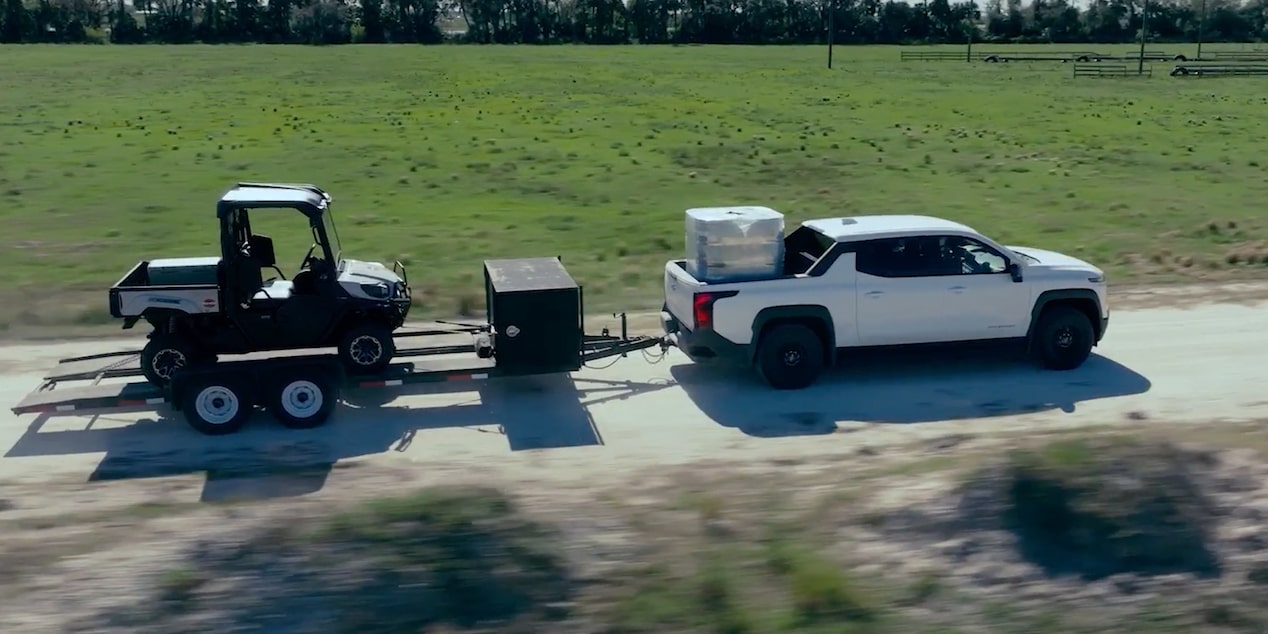 A Chevrolet Silverado pulling a trailer down a country road.