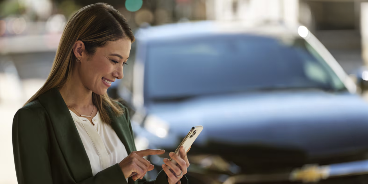 A Lady Using Her Phone with a Chevy Vehicle Behind Her
