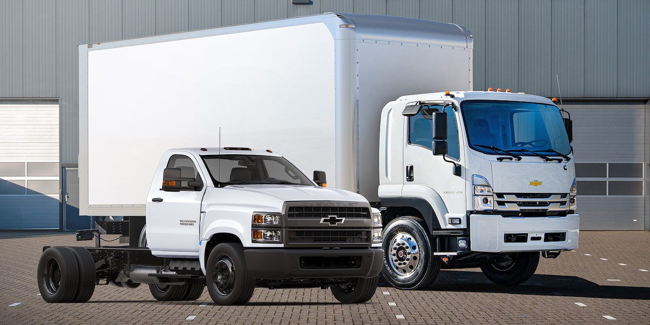 A cab forward Chevrolet and a chasis cab truck parked in front of a building.