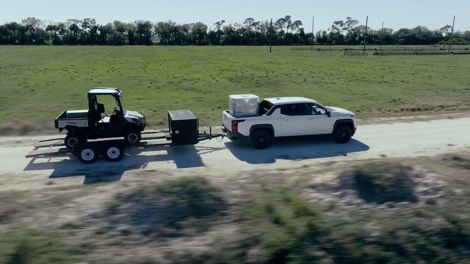 A 2025 GM Silverado EV pulling a trailer down a country road.