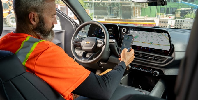 A driver behind the wheel of a Silverado EV checking vehicle status on their phone. 