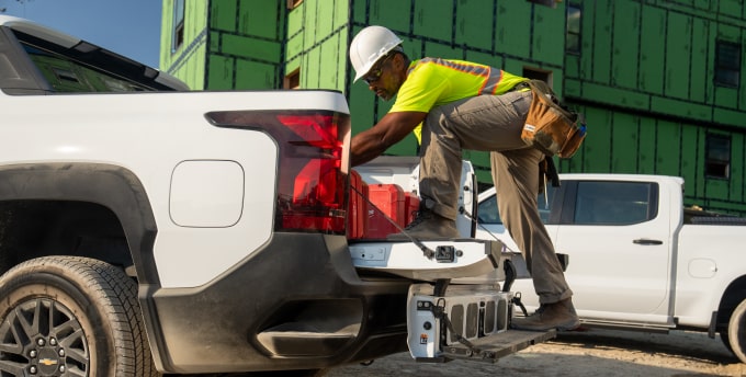 A construction worker climbing into the bed of a Silverado EV.
