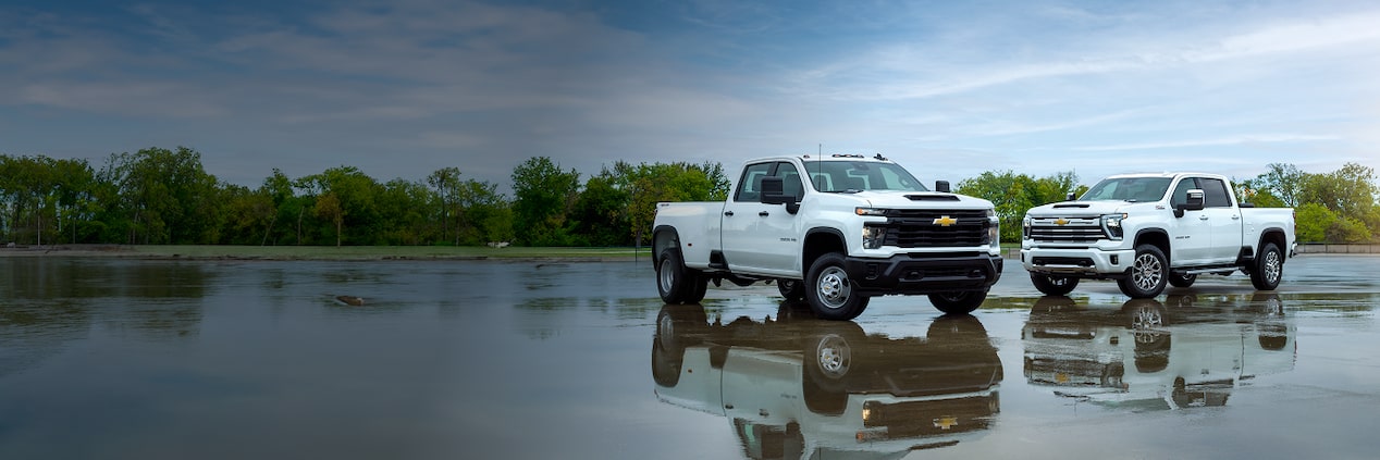 Two white Chevrolet Silverados parked in a empty wet parking lot. 