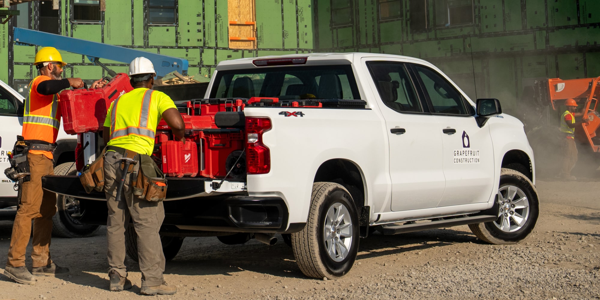 Two construction workers unloading tools from the bed of a white Chevrolet Silverado fleet truck. 