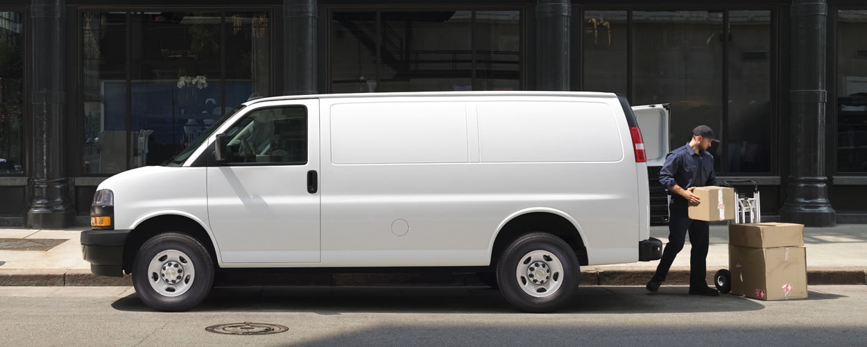 Chevrolet Express Cargo Work Van in side view, as a delivery driver removes packages from the rear