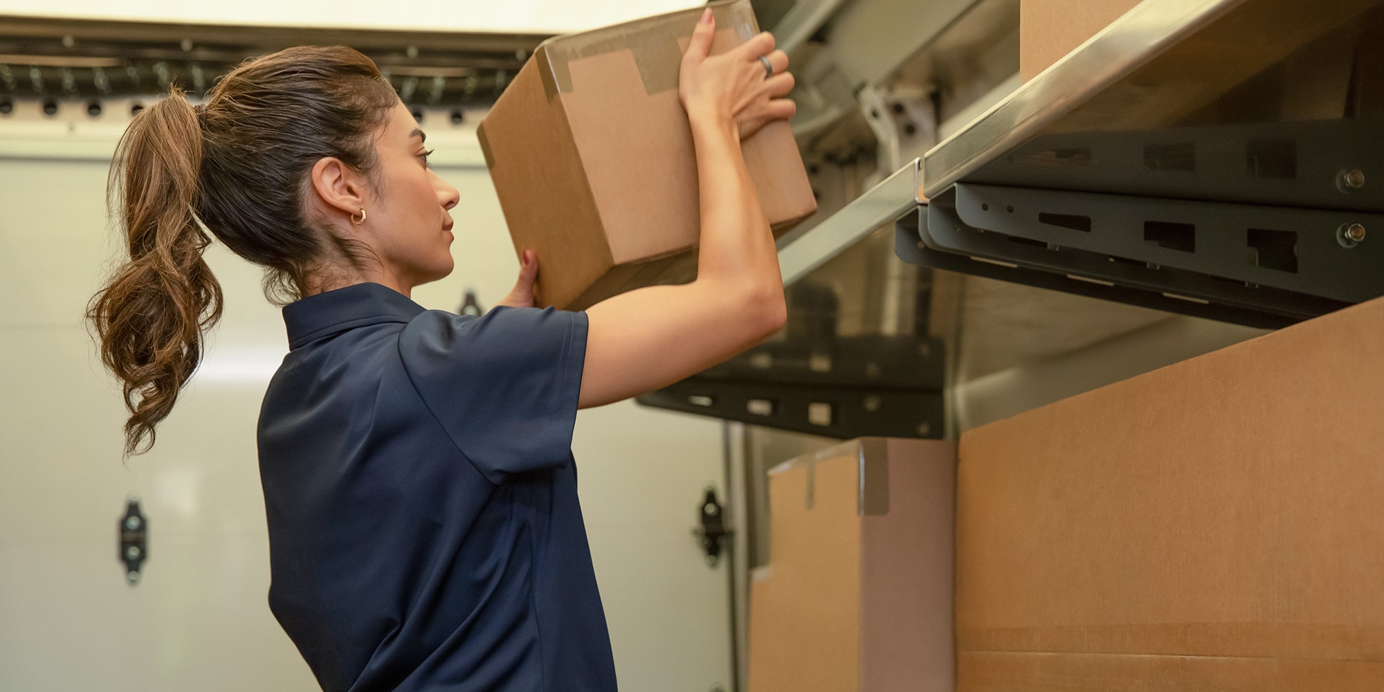 A delivery driver placing a package on the high shelf in the cargo by of a BrightDrop Zevo delivery vehicle.