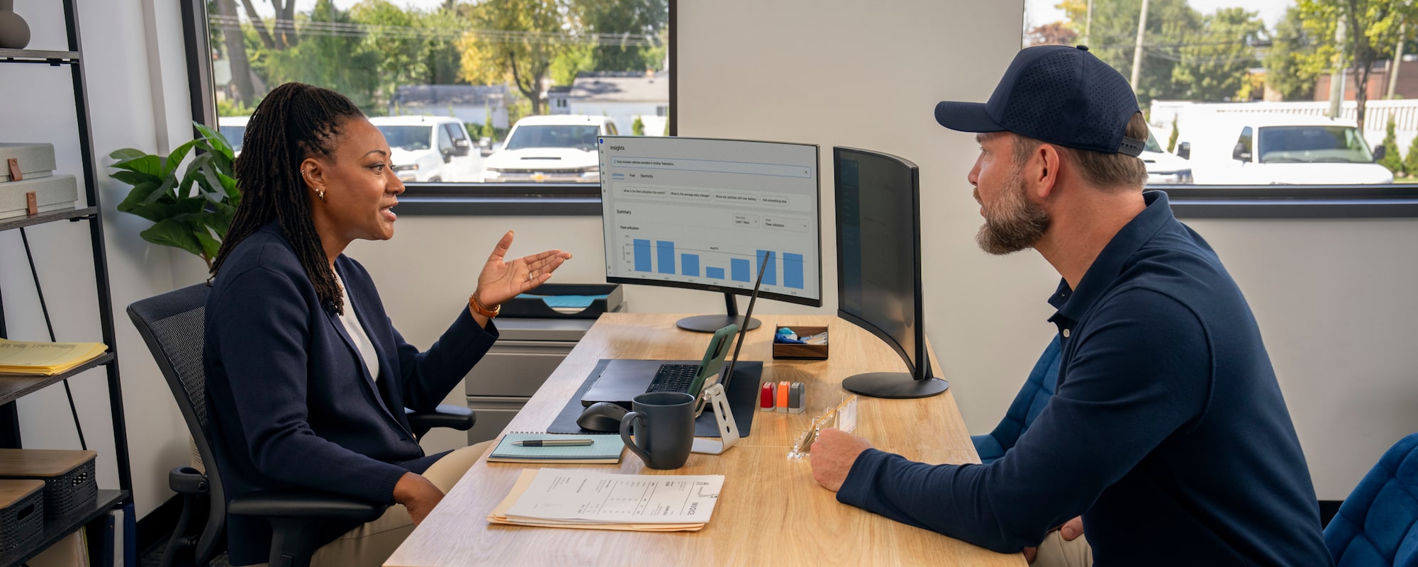 Two workers speaking in an office with OnStar vehicle insights on the computer monitor
