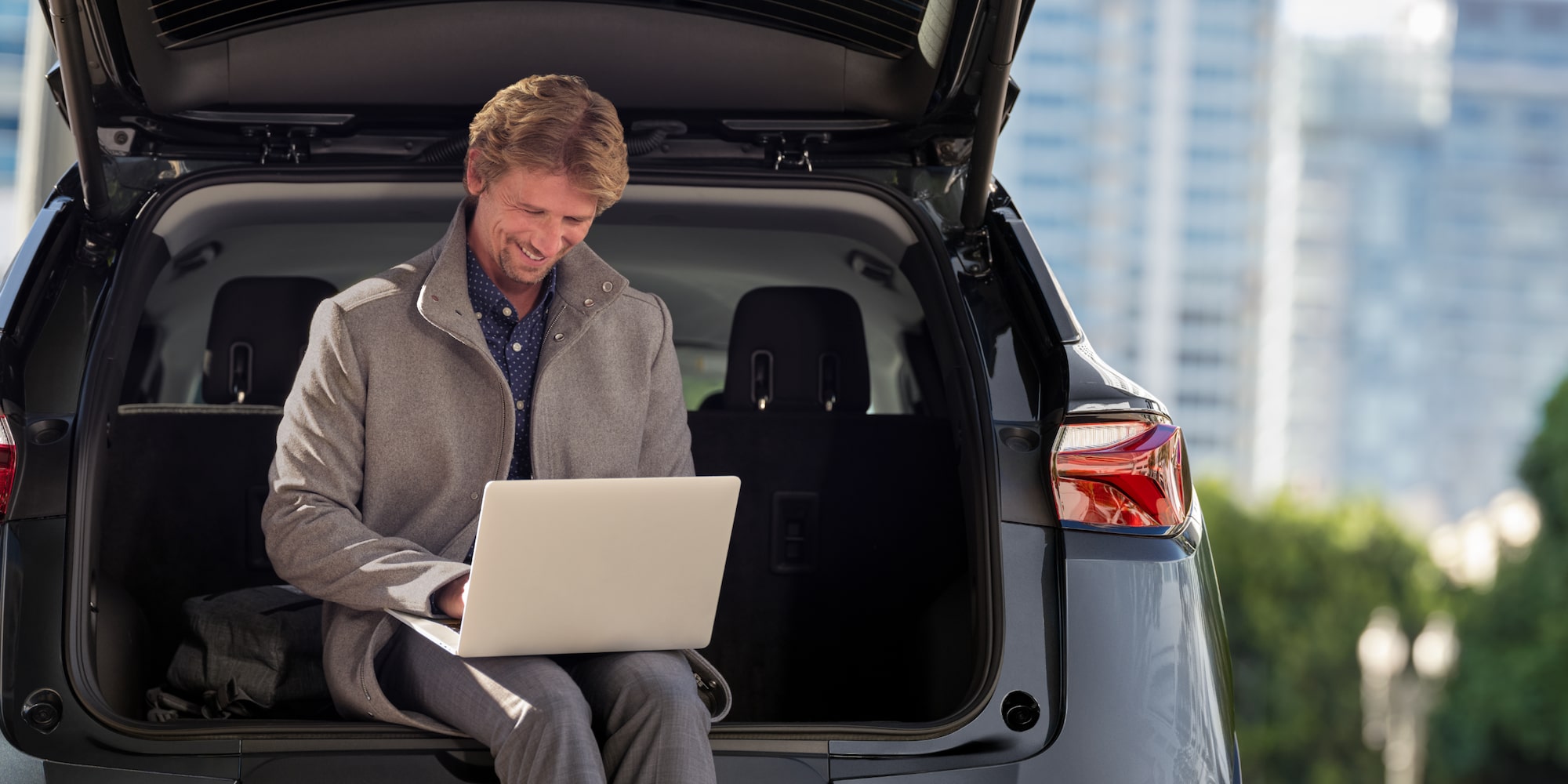 A man using his laptop and the in vehicle wifi while sitting on the tailgate of his Chevrolet Blazer. 