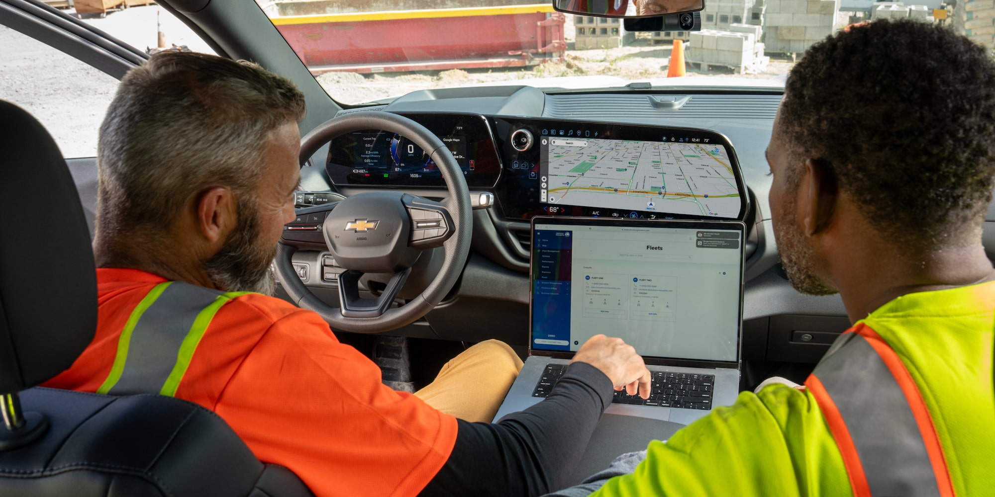 Two workers using a laptop and the infotainment system in their Chevrolet Silverado. 