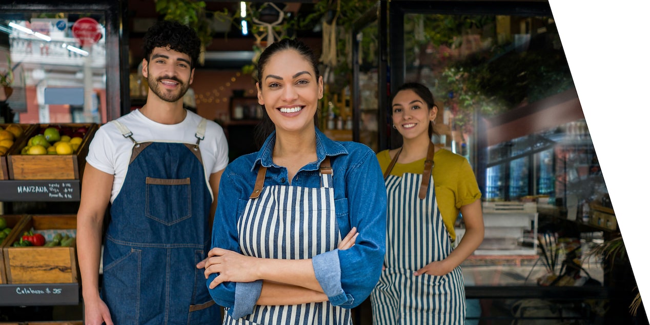 3 people wearing aprons in front of their market.