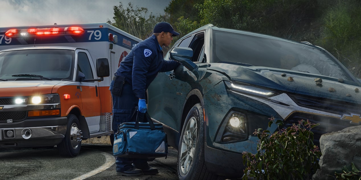 An emergency responder looking through the passenger side window of a crashed car. 