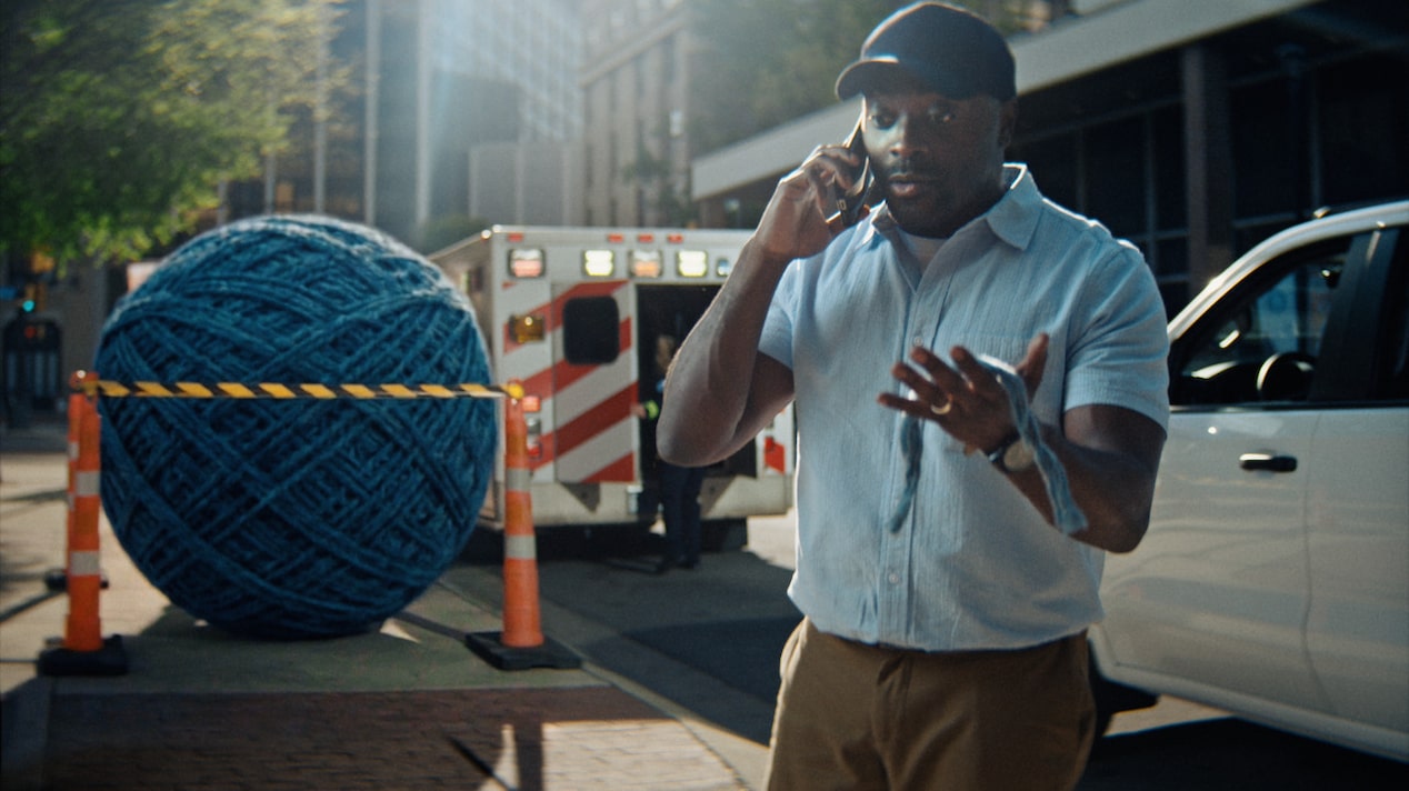 A man on the phone in front of a giant ball of string and an ambulance.